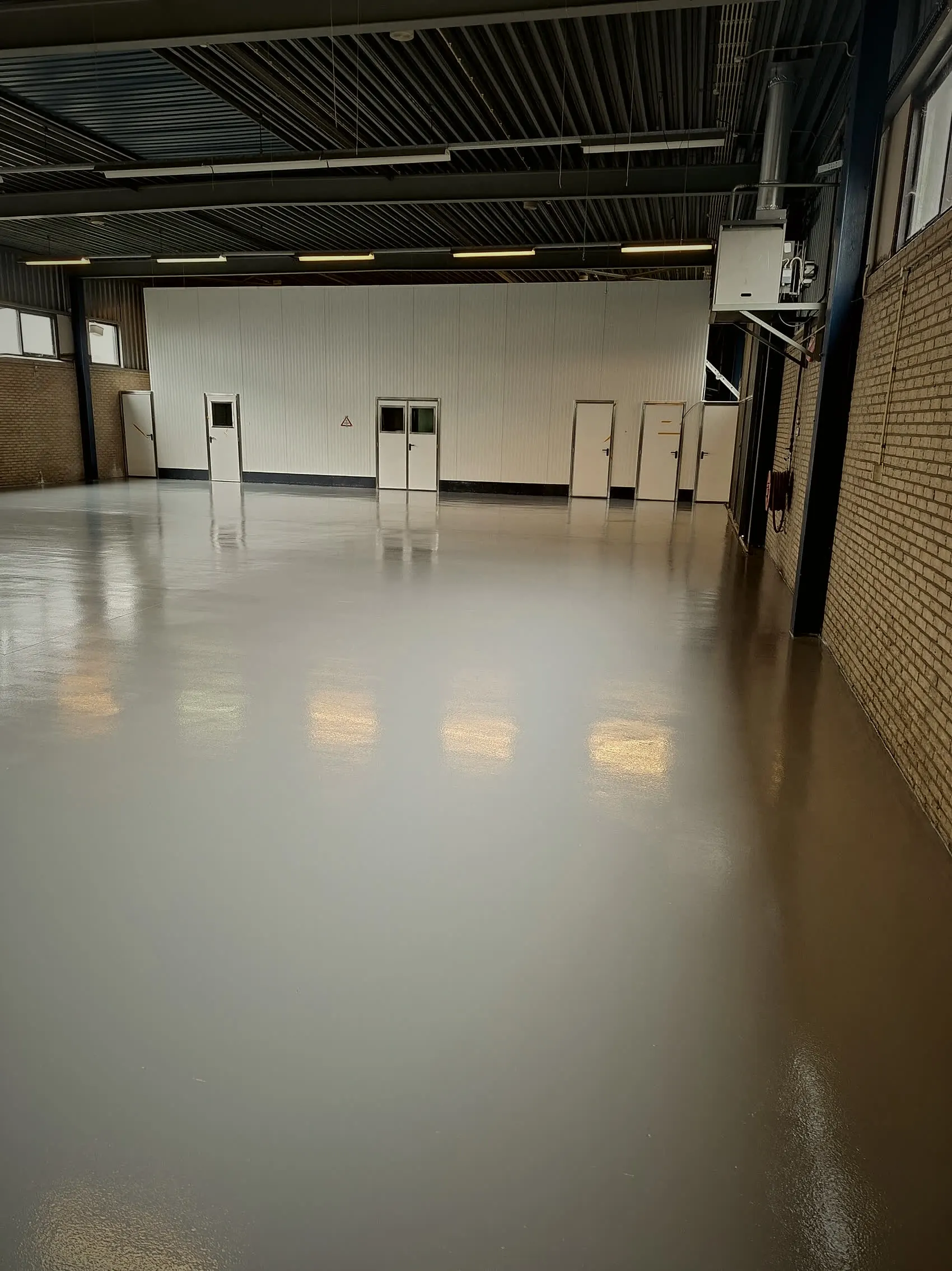Lege bedrijfshal met lichtgrijze epoxyvloer waarin de verlichting doorloopt