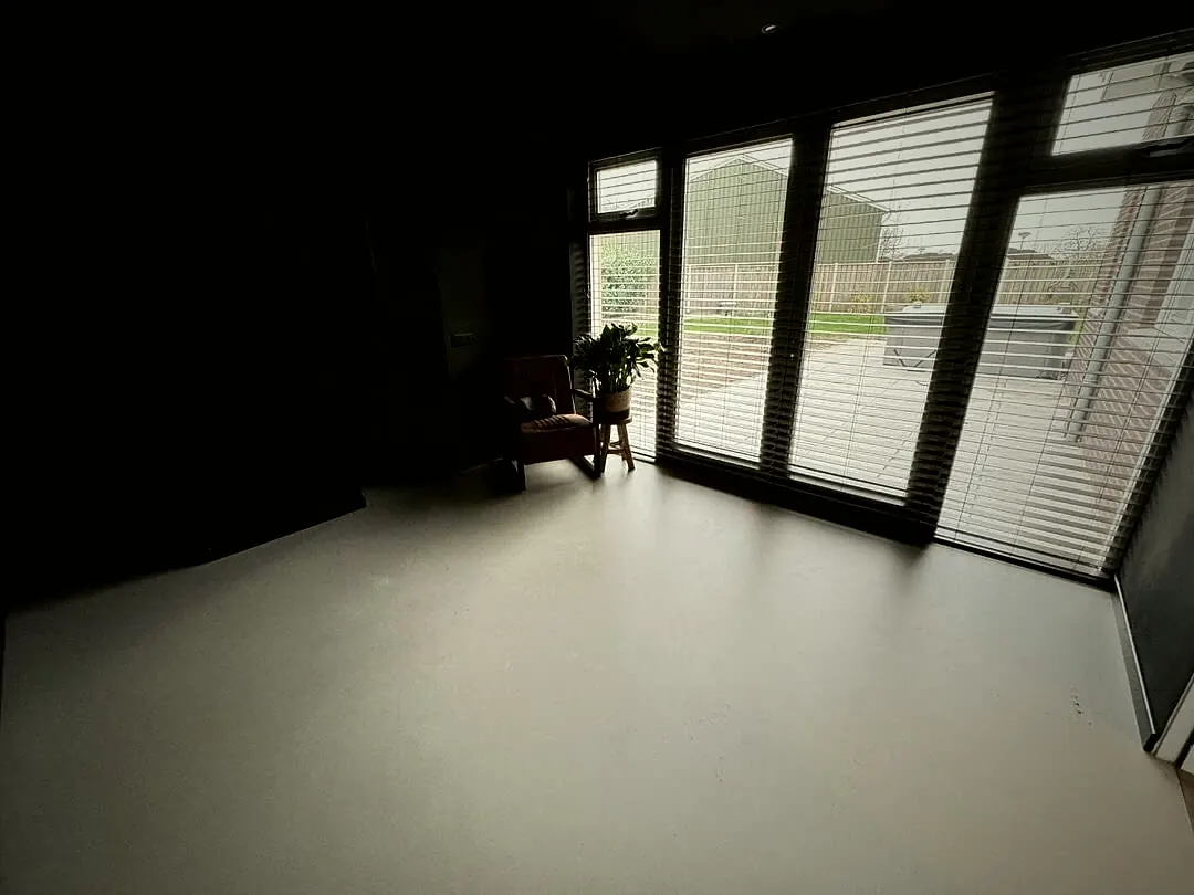 Woonkamer met lichte PU gietvloer en donkere wanden langs een raampartij