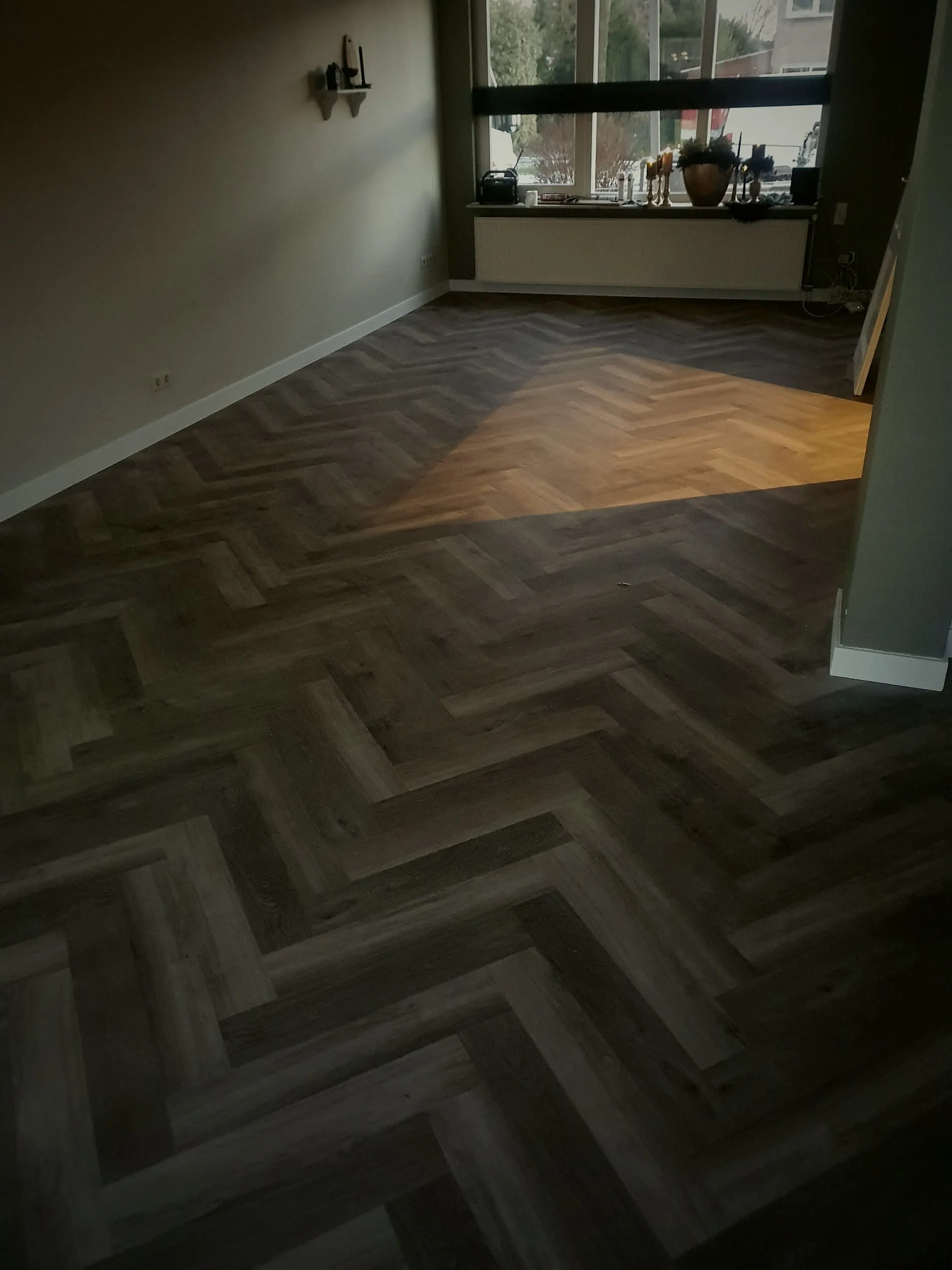 Woonkamer met donkere visgraat PVC vloer langs een groene wand